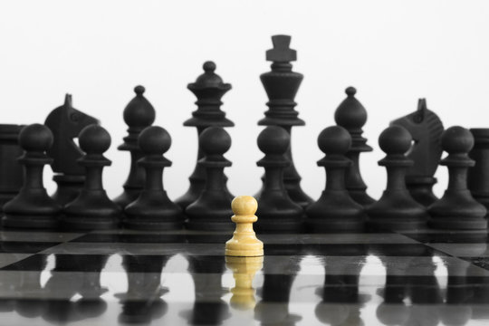 Self confidence white peon standing in front of a black chess army before confrontation