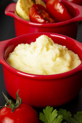 Food is still life. Two red pots with potato puree and fried vegetables on a black tray. Background black marble.