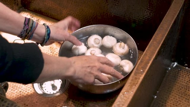 Close up of a person rinsing white mushrooms in a bowl with fresh water