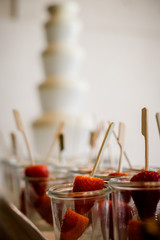 Strawberries in glass with fondue fountain in background.