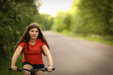Fototapeta na wymiar teenager girl with long brown hair ride bicycle on country road through the forest close up photo