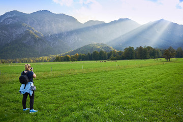 Naklejka na ściany i meble Ein Mädchen macht das Fotos von Bergen in den Alpen. Grünes Gras, Sommer und schöne Aussicht.