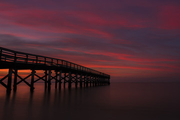 Fototapeta na wymiar Dramatic red sunset viewed from Bayshore Waterfront Park, New Jersey featuring fishing pier on the background