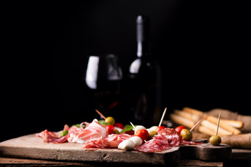 Assorted meats and  cherry mozzarella cheese, on a wooden cutting board with bottle of wine and glass on background. Italian antipasti