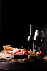 Fototapeta na wymiar Assorted meats and cherry mozzarella cheese, on a wooden cutting board with bottle of wine and glass on background. Italian antipasti