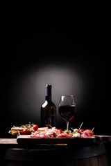 Assorted meats and  cherry mozzarella cheese, on a wooden cutting board with bottle of wine and glass on background. Italian antipasti