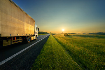 Truck driving on the asphalt road in a rural landscape in the golden sunset
