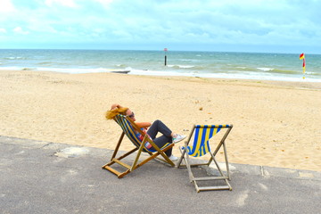 Blond girl sitting on a deck chair on the beach, Bournemouth, England, June