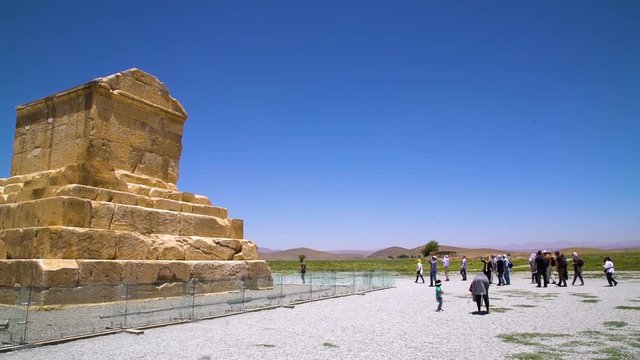 A steady wide shot of the Tomb of Cyrus while people walk in front of it.