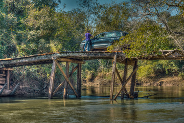Tourist with car on a large, rickety wooden bridge in the middle of the wilderness of Paraguay.