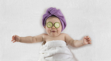 Funny baby girl wrapped in white towel with cucumbers on her eyes - 210381425
