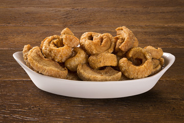 Pile of fried bacon cube portion in a white plate on wood background.
