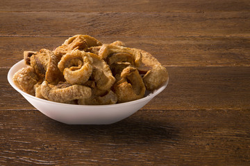 Pile of fried bacon cube portion in a white plate on wood background.