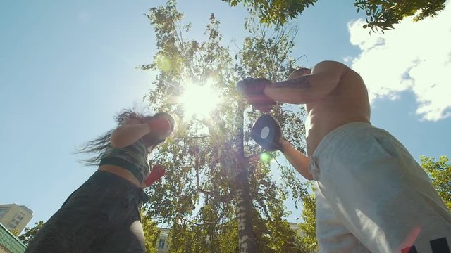 Young muscular man with attractive woman engaged in boxing outdoors at summer day