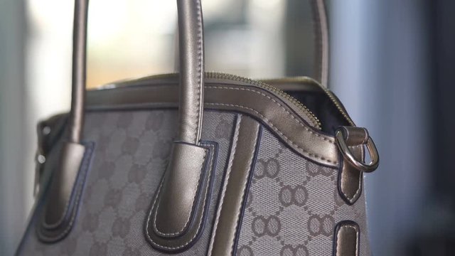 Closeup of a woman hands closing the zipper of a ladies handbag
