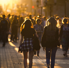 Two young women walking in crowd on the pedestrian street at summer sunset