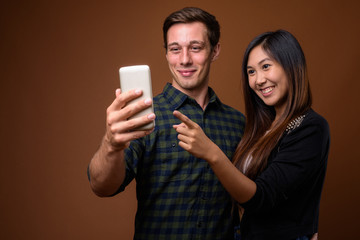 Studio shot of young multi-ethnic couple together against brown 