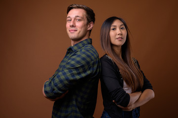 Studio shot of young multi-ethnic couple together against brown 