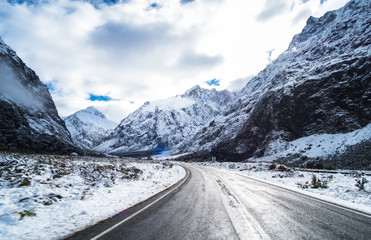 The stunning scenery of a rocky mountain and trees covered with a white snow. A road to Milford Sound. A filmed while driving.