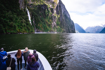 A group of tourists enjoying a stunning scene of nature while cruising into waterfall in Milford Sound, New Zealand. - obrazy, fototapety, plakaty