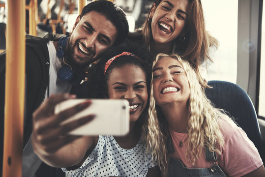 Laughing group of friends taking selfies together on a bus