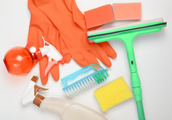 House cleaning products.  Window mop, sponge, bottle of spray, yellow latex gloves, brush on white...