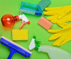 House cleaning products.  Window mop, sponge, bottle of spray, yellow latex gloves, brush on green background. Top view. Flat lay style.