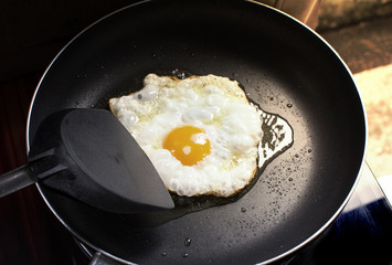 Fried sunny side up egg in a black hot pan and plastic spade at kitchen in home.