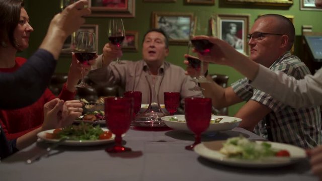 People sit at a table in the restaurant clink glasses and drink red wine
