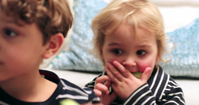 Cute adorable child starring at screen while chewing and eating cucumber. Candid real life authentic baby with red cheaks
