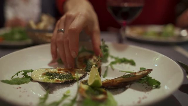 Plate with oven cooked mussels in the sink. Female hand takes the Medes
