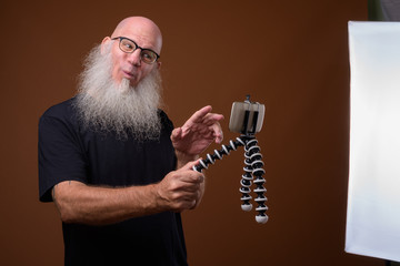 Mature bald man with long gray beard against brown background