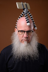 Mature bald man with long gray beard against brown background