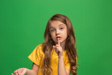 The young teen girl whispering a secret behind her hand over green background