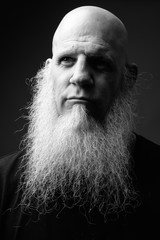 Mature bald man with long beard against gray background in black