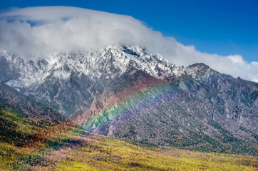 Mountains landscape with rainbow- cloudy sky in pastel colors for your design. Romantic seascape - seaside view with silhouettes of blue hills in a fog and fall forest