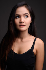 Fototapeta premium Young beautiful Asian woman thinking against gray background
