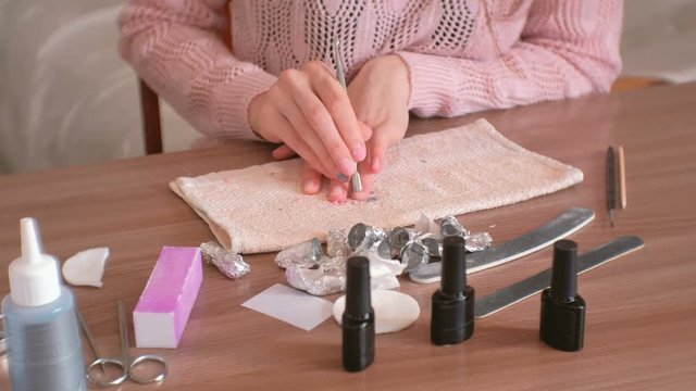 Removing gel Polish from nails. Woman removes shellac from nails with pusher. Close-up hand. Manicure tools on the table.