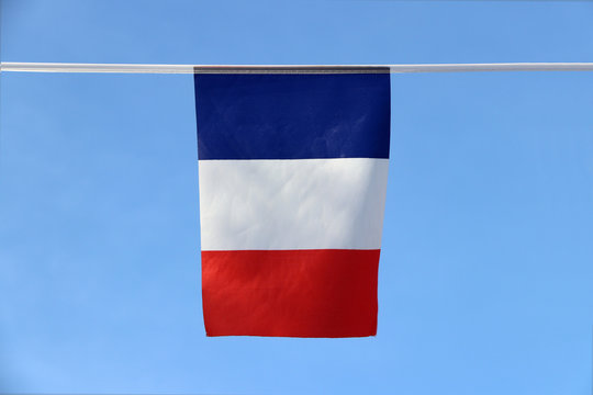 Mini fabric rail flag of France it is a tricolor flag featuring three vertical bands colored blue white and red, hanging on the rope cloth on blue sky background.