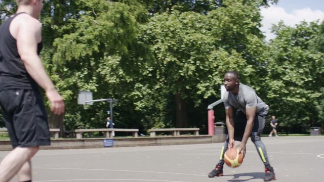 Men playing a game of basketball on an outdoor court in summer