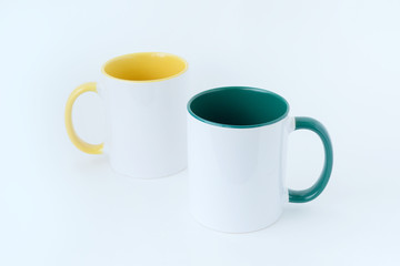 Two white mugs, with a green and yellow handle on a white background.  Isolated.   View from above.