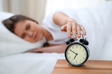 Sleepy young woman stretching hand to ringing alarm willing turn it off. Early wake up, not getting...