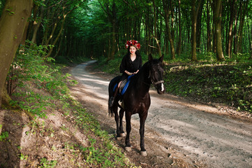 Mystical girl in wreath wear in black at horse in wood.