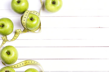 Green apples and yellow centimeter tape on white wooden background with space for text, top view.