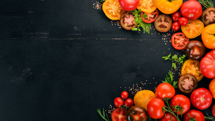 Assortment of colored fresh tomatoes. On a black wooden background. Top view. Copy space.