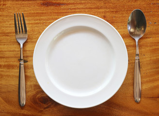 Empty plate on wooden table with fork and spoon