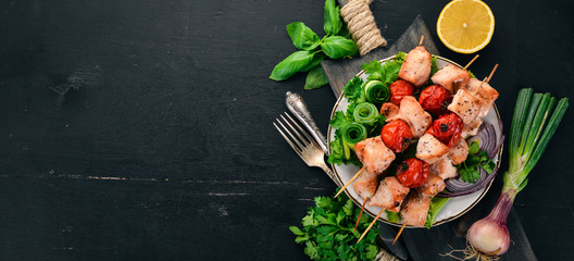 Chicken shish kebab with cherry tomatoes, and vegetables. On a wooden background. Top view. Copy space.