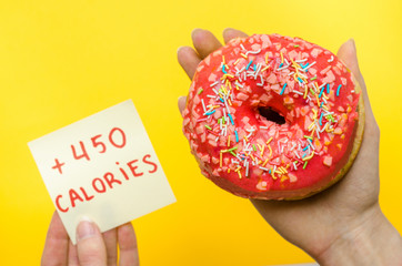 Female hand holding pink donut with sprinkles extra calories fat fast food excess weight unhealthy...