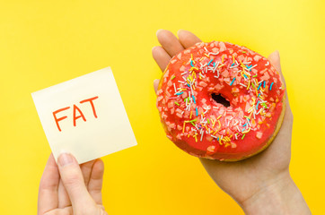 Female hand holding pink donut with sprinkles extra calories fat fast food excess weight unhealthy...