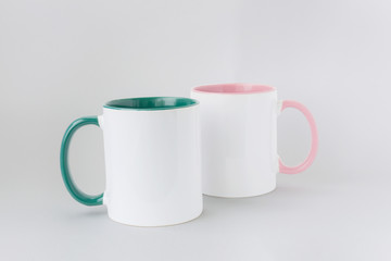 Two white mugs, with a green and pink handle on a light background. Isolated.